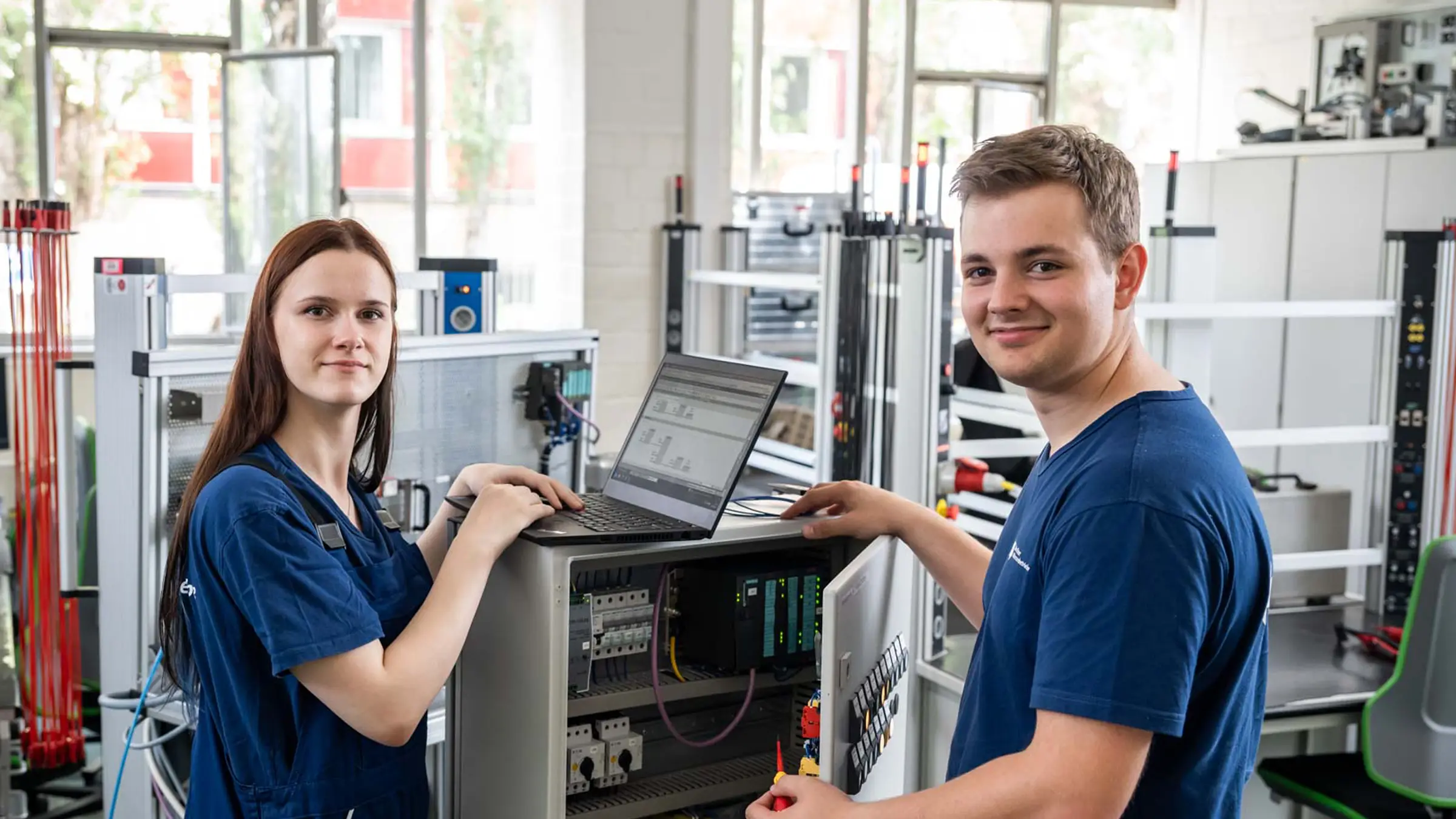 Zwei Auszubildende als Elektroniker:in für Automatisierungtechnik stehen an einem Laptop