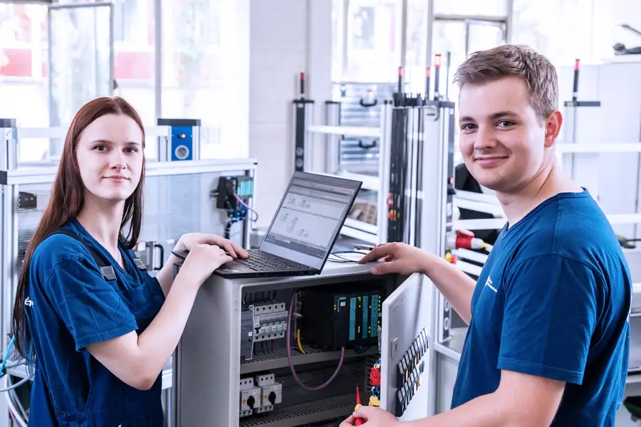 Auszubildende als Elektroniker:in für Automatisierungstechnik stehen an einem Laptop